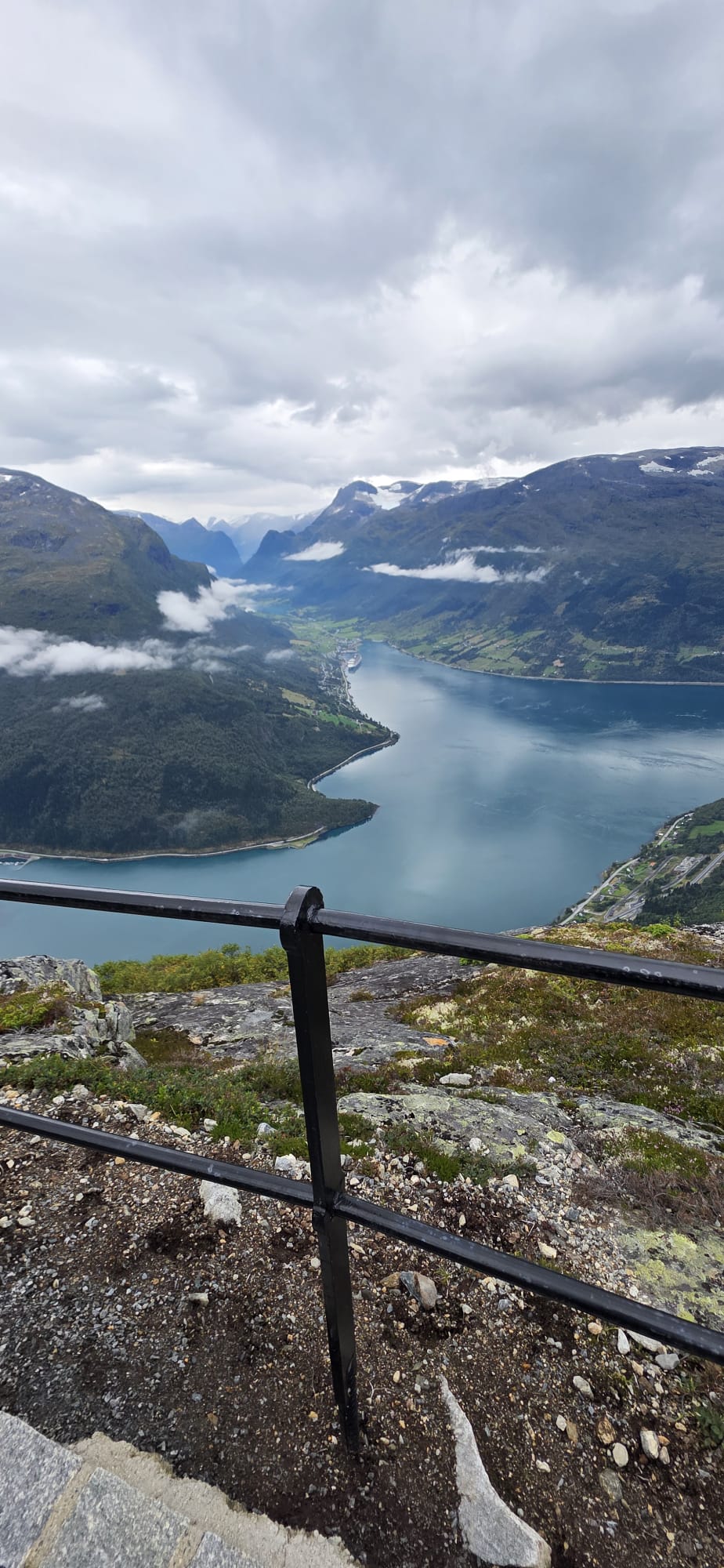 A viewpoint with railings looking down over a Norwegian fjord framed by low cloud and mountains
